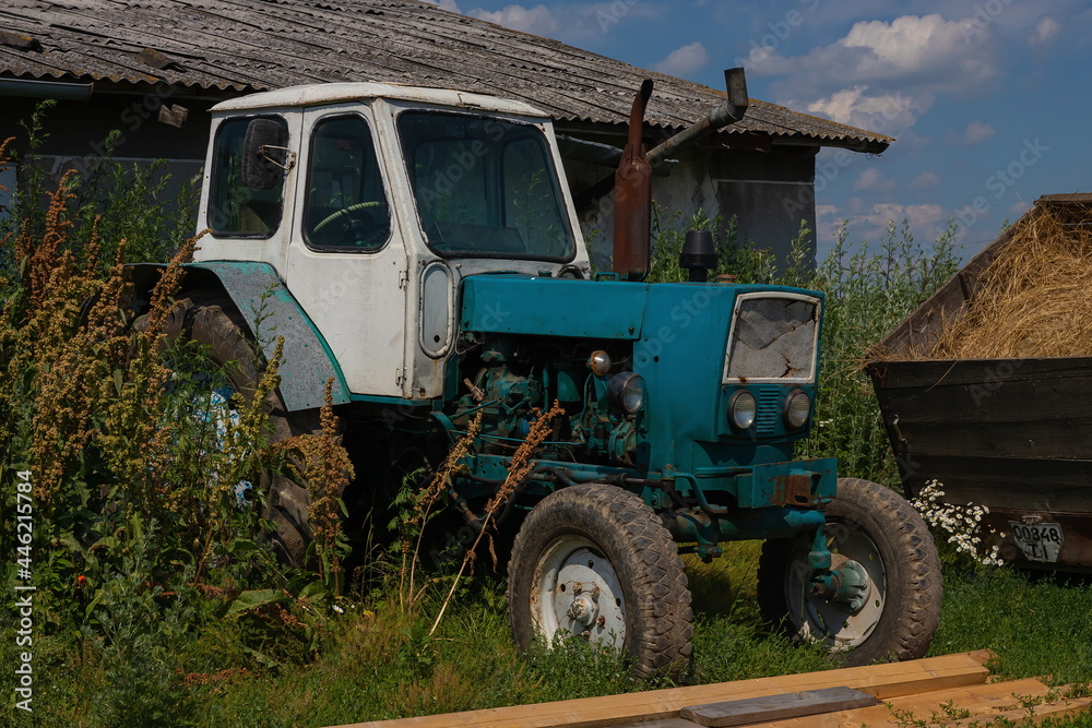 Obraz premium old tractor on a farm in the grass under the wall. blue sky, summer.