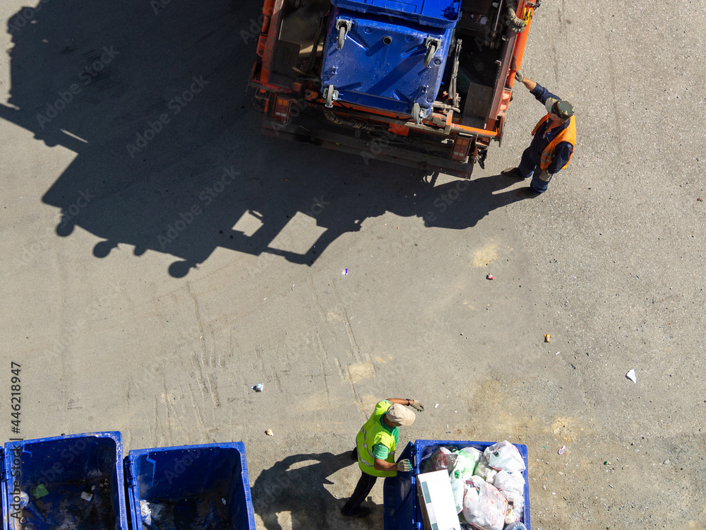 Garbage collection process top view. Men in gloves roll trash cans to a garbage truck.