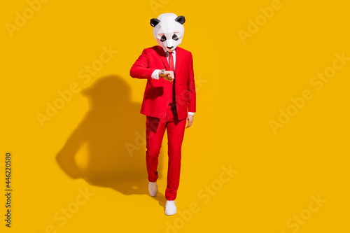 Photo of busy reliable panda guy walk look watch wear mask red suit tie sneakers isolated on yellow color background