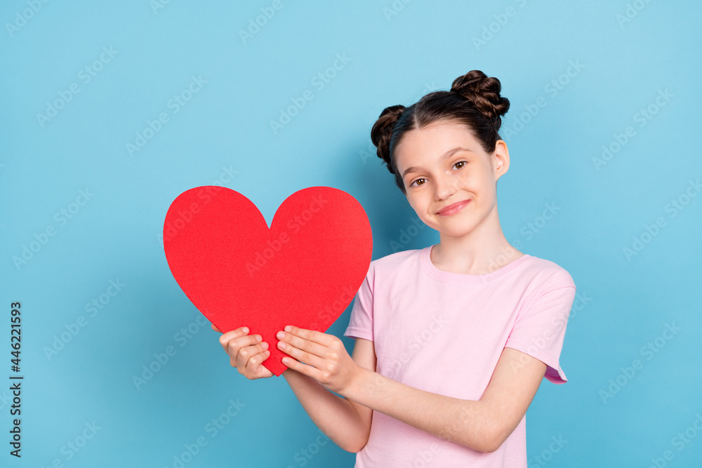 Photo of cheerful young happy positive little girl hold hands red paper heart isolated on blue color background Photo of cheerful young happy positive little girl hold hands red paper heart isolated on blue color background