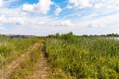 On a sunny summer day, a field road runs along a small lake, the city of Yelabuga, Tatarstan, Russia is visible on the horizon on a high hill on the left.