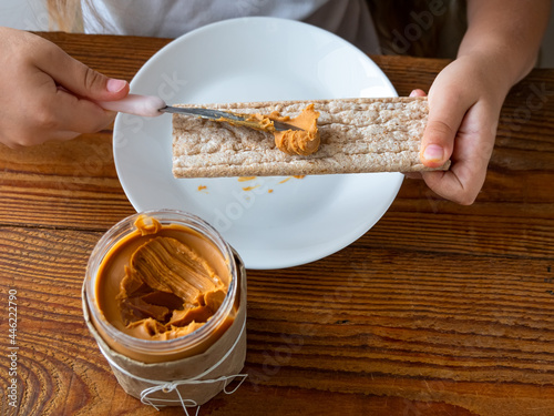 Fotografie Child spreading peanut butter on crispbread eating sandwich wooden table home kitchen