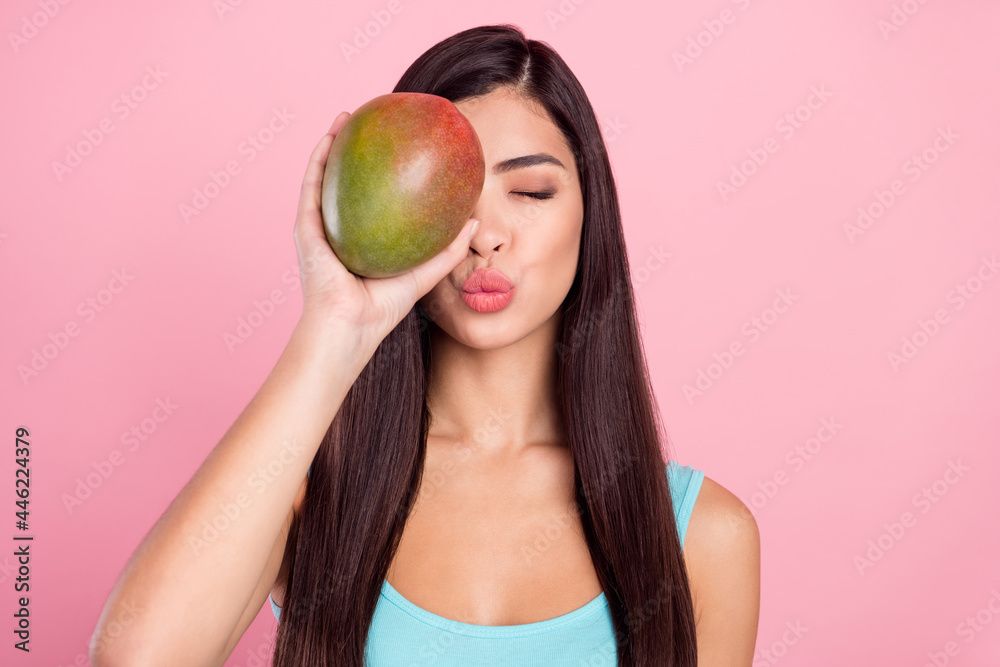 Photo portrait woman sending air kiss keeping exotic fruit covered face eye isolated pastel pink color background Photo portrait woman sending air kiss keeping exotic fruit covered face eye isolated pastel pink color background