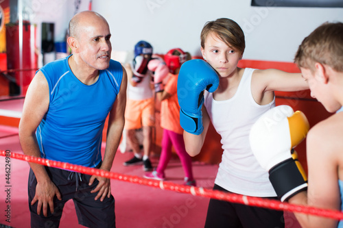 Young boxing children exercising with coach on boxing ring at gym
