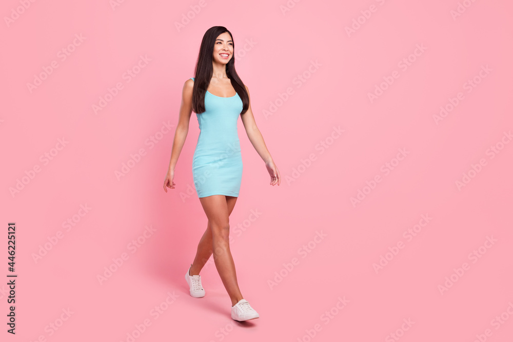 Full size photo of optimistic lady go look empty space wear blue dress sneakers isolated on pink color background Full size photo of optimistic lady go look empty space wear blue dress sneakers isolated on pink color background