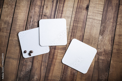 Photo of three blank white square beer coasters and coffee beans on wood table background. Top view. Flat lay.
