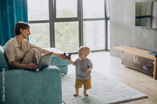 Mother eorking on laptop while son playing video games photo