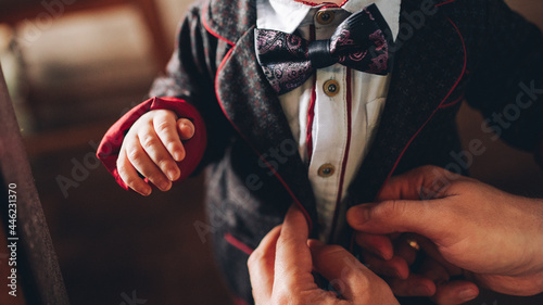 Parent buttons a jacket to a small child in a business suit with a bow tie (ID: 446231370)