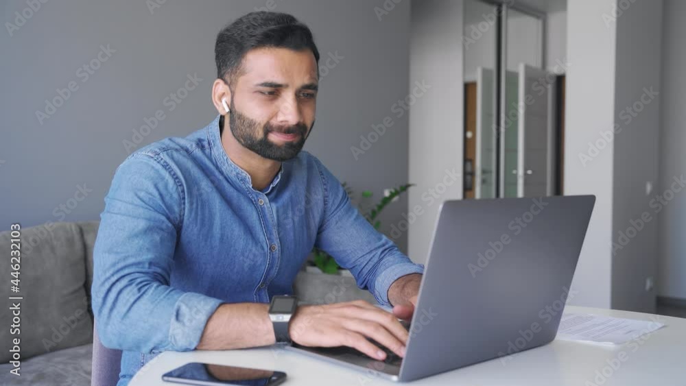 Young adult smiling indian businessman working on laptop computer at home office