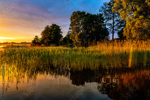 Panoramic summer sunset view of Jezioro Selmet Wielki lake landscape with vintage pier, reeds and wooded shoreline in Sedki village in Masuria region of Poland