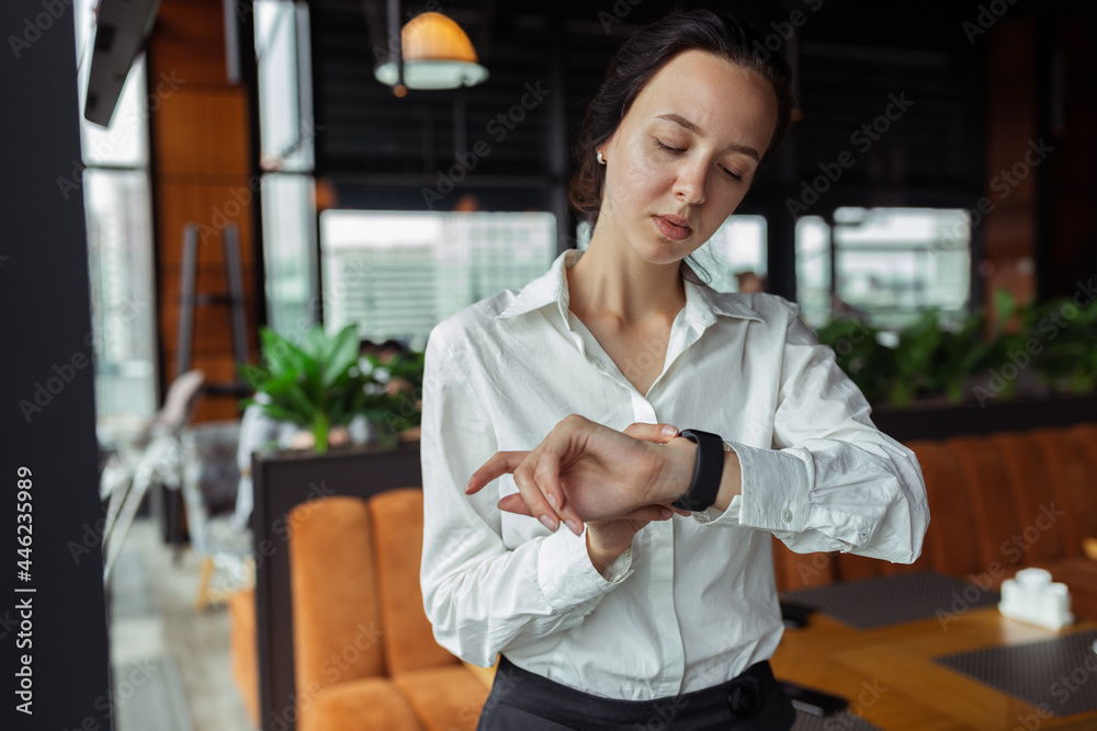 Serious elegant businesswoman checking time on wristwatch and waiting for meeting in cafe Serious elegant businesswoman checking time on wristwatch and waiting for meeting in cafe