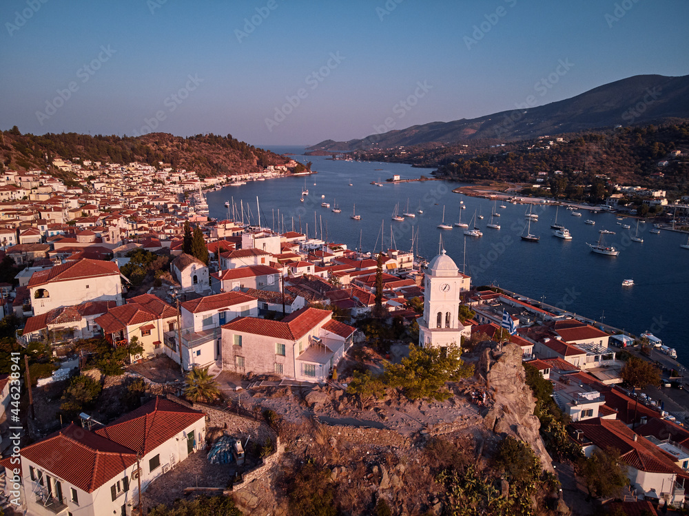 Drone view of Poros island. Clock tower in old town with traditional white houses near the sea. Saronic gulf, Greece, Europe.