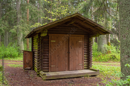 Wooden public toilet in the Estonian forest near the public rest and barbeque RMK area on a cloudy summer day. © Aimur