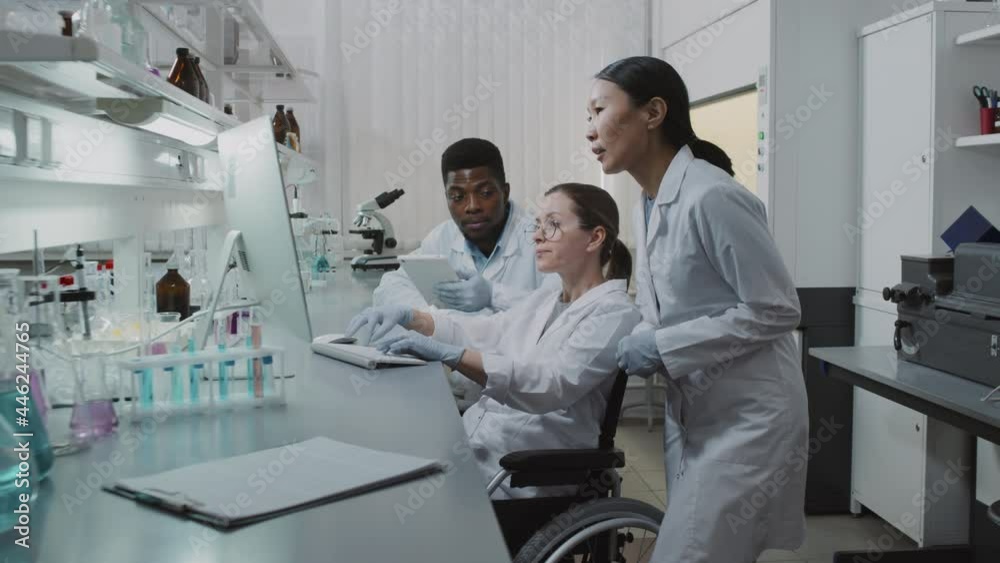 Slowmo tracking shot of diverse team of scientists looking at computer screen and discussing research in lab