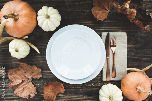 Holiday place setting with plate, napkin, antlers and silverware on a Thanksgiving Day decorated table shot from flat lay or top view position. Pumpkins, antlers and fallen leaves. 