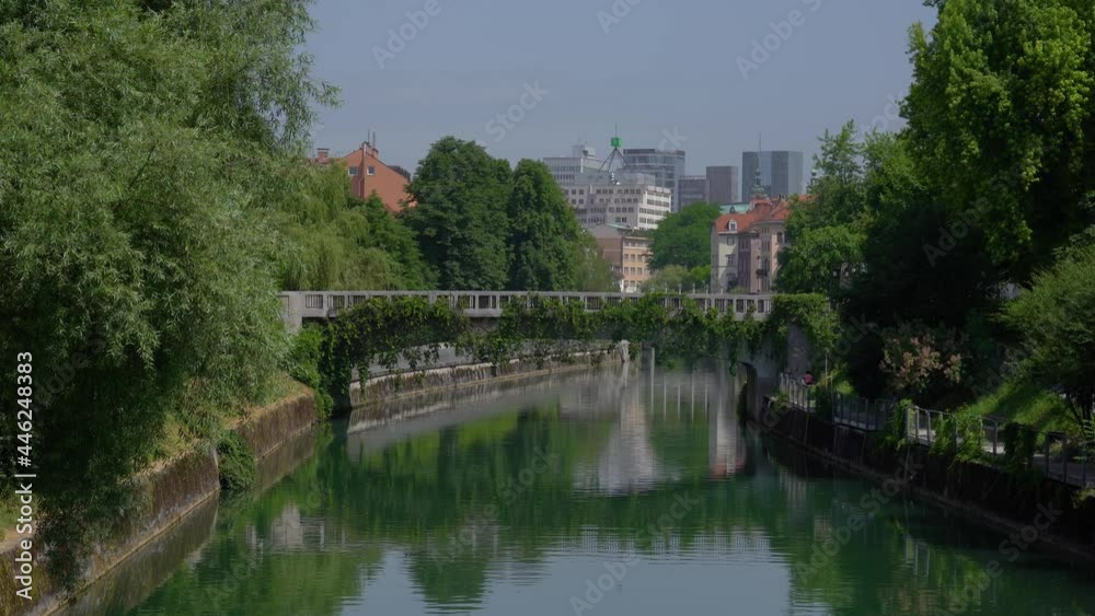 View of St James Bridge and green Ljubljanica river in Ljubljana city, Slovenia. Sunny weather in summer. People walking on the bridge. Handheld, real time, wide angle View of St James Bridge and green Ljubljanica river in Ljubljana city, Slovenia. Sunny weather in summer. People walking on the bridge. Handheld, real time, wide angle