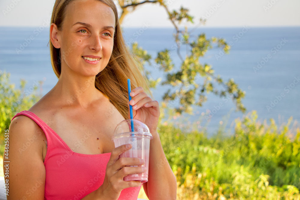 Vegan woman in pink dress is relaxing near sea cost with berry smoothie
