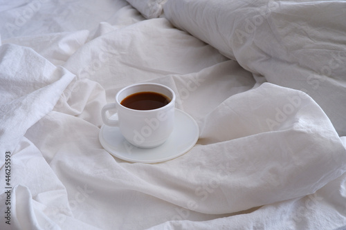 A cup of black coffee in a white bed. Breakfast in bed. Interior.