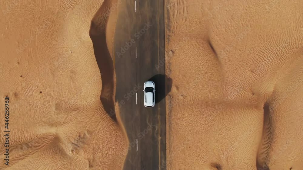 Vertical panning from a quadcopter. White car is driving on road in the desert