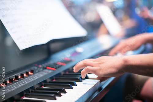 The musician's fingers play the keys on the synthesizer against the background of bokeh.