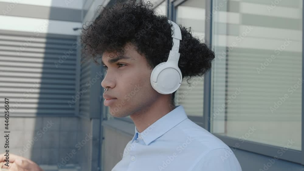 Caucasian happy beautiful mixed race male in headphones and listening to music outdoors. Joyful guy in good mood enjoying songs in town. Close up portrait. Leisure concept Caucasian happy beautiful mixed race male in headphones and listening to music outdoors. Joyful guy in good mood enjoying songs in town. Close up portrait. Leisure concept