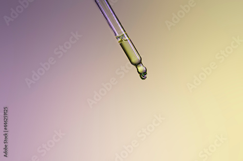 Liquid serum and dropper on purple and yellow background. Front view..