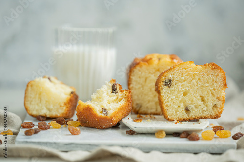 Homemade freshly baked butter sponge cake with raisins on white table with glass of milk. Sweet bakery - beautiful breakfast, macro shot, close up view with copy space. Biscuit dessert.