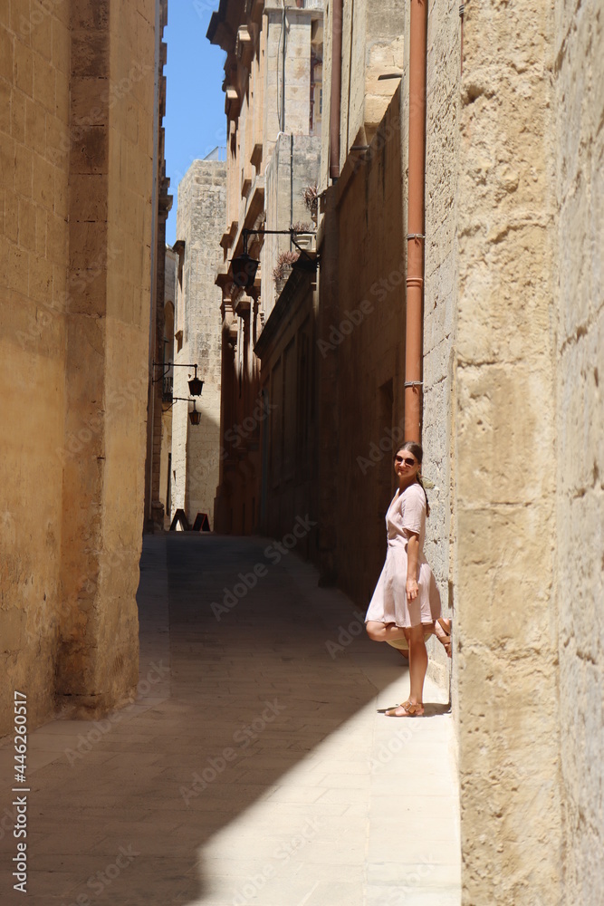 Woman in long dress walking old town of Valletta, sands and ruins tiny square streets