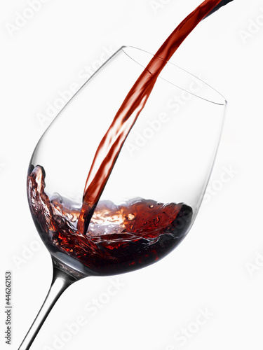 Red wine pouring into a wine glass, with a white background