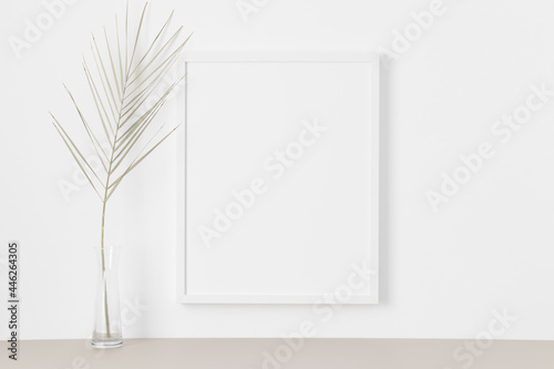 White frame mockup on the wall with a palm leaf.