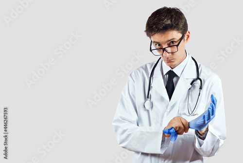 Doctor with a stethoscope on a white background. A man in a medical gown with glasses. The doctor wears blue gloves.