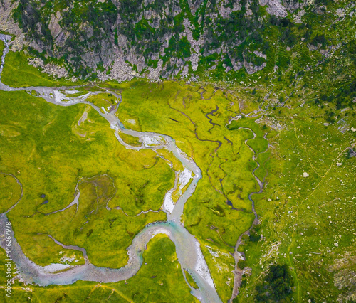 Aerial vertical drone view of a river flowing through a green valley.
