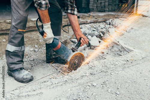 A worker with a grinder cuts the concrete pavement of the road and sparks fly. Construction and repair of the roadway.