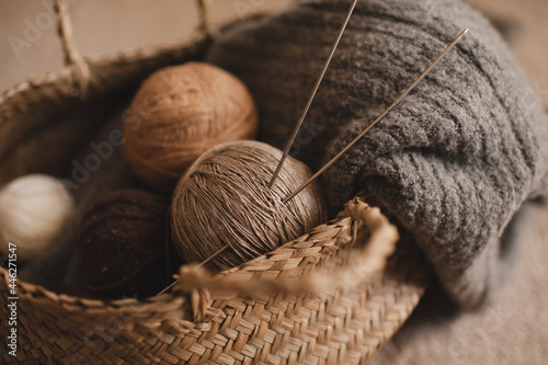 Yarn balls with knit cloth fabric and .knitting needles in straw basket in room. Winter season. Cozy warm home atmosphere.