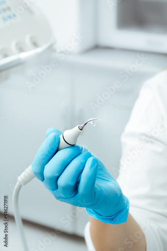 Dental ultrasonic scaler with water splash. Periodontal ultrasonic scaler. Dental instrument. Tartar removal. Dentist in blue gloves.