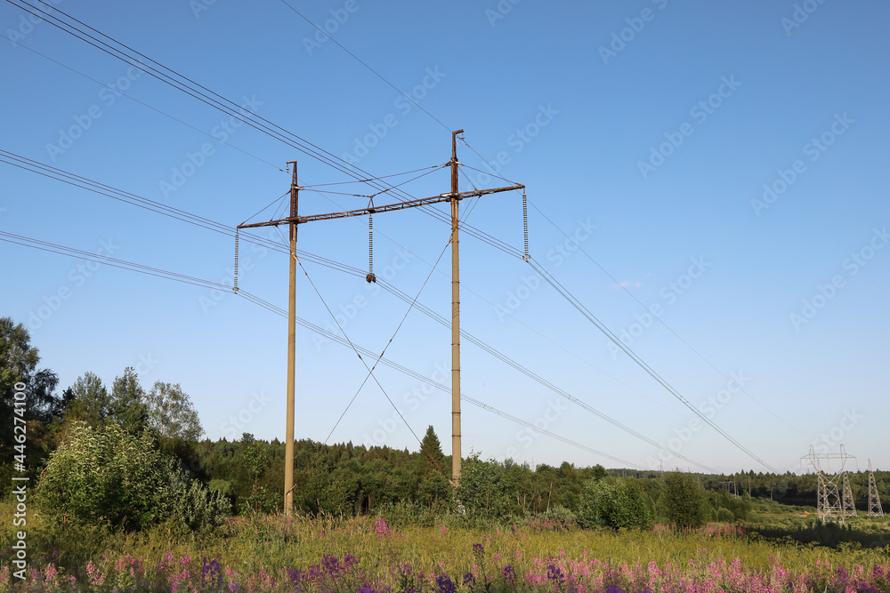 Polls of high-voltage power line on background of blue sky in rural areas on summer day