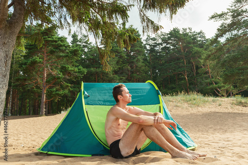 Young man sitting by tent ant posing