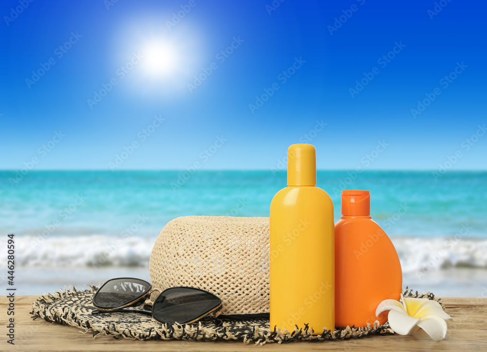 Bottles of skin sun protection products and beach accessories on wooden table against seascape. Space for design