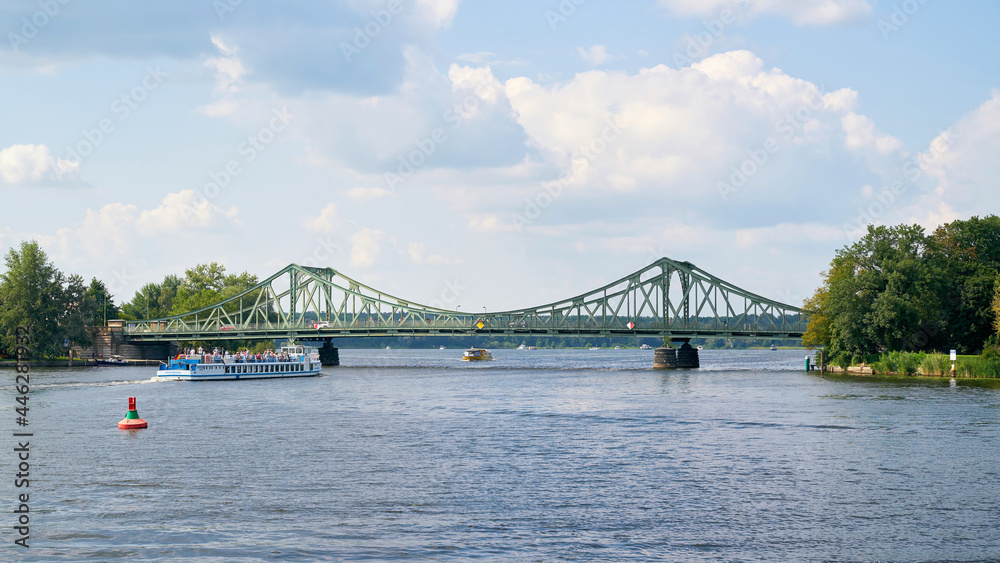 Naklejka premium Die Glienicker Brücke über den Fluss Havel zwischen Potsdam und Berlin. Im Vordergrund ein Ausflugsschiff mit Touristen.