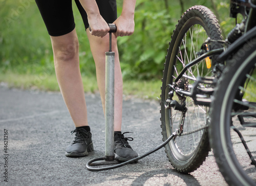 A girl pumps a bicycle wheel with a pump. Bicycle repair in the forest. Close up