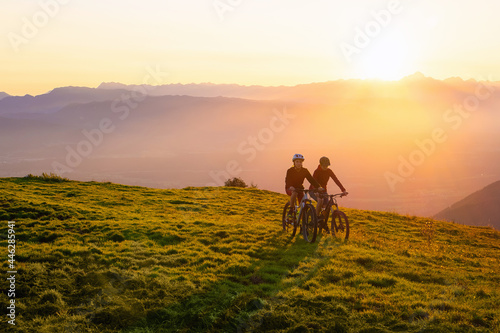 Mother and daughter cycling on mountain bikes at a sunset in mountains.