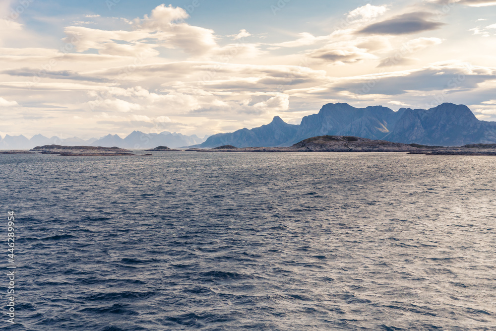 Stormclouds with sun shining through them above dramatic mountain range of Lofoten Islands, viewed from boat on the sea between Bodo and Moskenes. Dramatic landscape of Norwegian arctic.