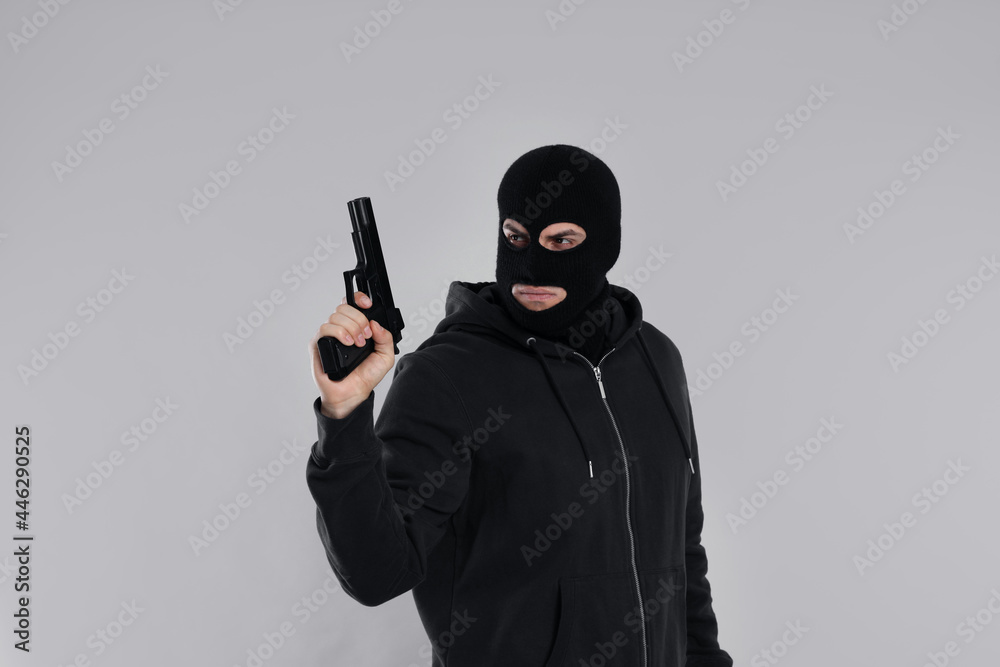 Man wearing black balaclava with gun on light grey background Man wearing black balaclava with gun on light grey background