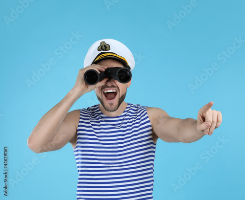 Sailor looking through binoculars and pointing on light blue background