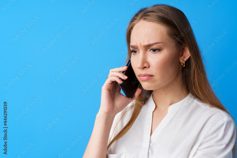 Unhappy woman talking on the phone stressed with bad news, blue background Unhappy woman talking on the phone stressed with bad news, blue background