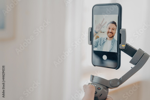 Male hand holding gimbal stabilizer with smartphone and smiling at camera