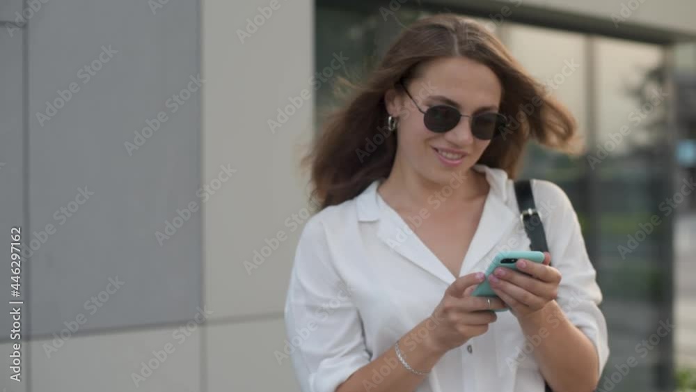 Portrait of beautiful girl with brown hair standing on street, holding smartphone and looking at camera. Smiling woman in casual outfit spending leisure time with modern gadget. Portrait of beautiful girl with brown hair standing on street, holding smartphone and looking at camera. Smiling woman in casual outfit spending leisure time with modern gadget.