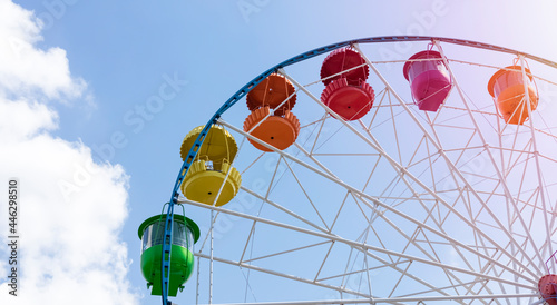 Panoramic view of the Ferris wheel at the amusement park. Colorful ferris wheel against the blue sky on a sunny day. Holiday and family vacation concept