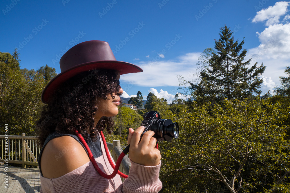 Young woman with hat and curly hair looking at lake with binoculars