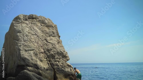 Young man climbs a high rock into the sea on a hot summer day to jump into the water